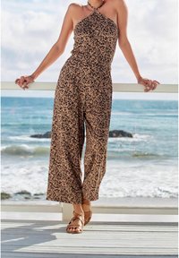 Mono de leopardo en tonos marrón y negro, diseño sin mangas, cuello halter, silueta de pierna ancha, combinado con sandalias de tiras color beige.