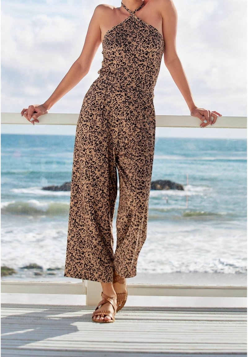 Mono de leopardo en tonos marrón y negro, diseño sin mangas, cuello halter, silueta de pierna ancha, combinado con sandalias de tiras color beige.