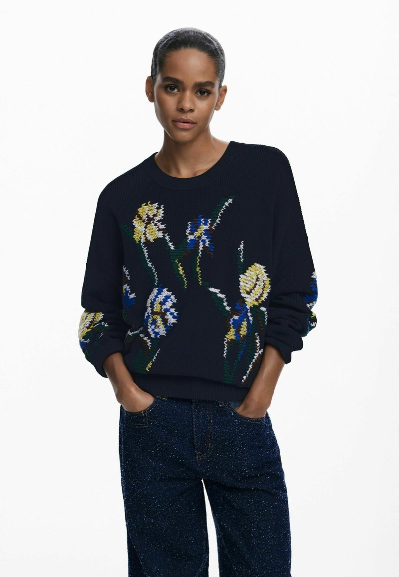Navy sweater with embroidered floral patterns in yellow, blue, and green, featuring a round neck and ribbed cuffs; paired with dark textured jeans.