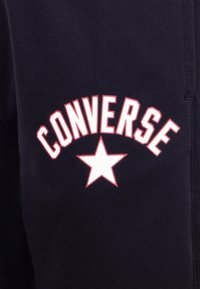 Sudadera azul marina con el texto "CONVERSE" en blanco y rojo arqueado sobre un gráfico central de una estrella blanca. Fabricada en un tejido suave con una textura lisa.
