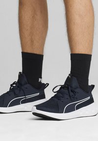 Nawodne buty sportowe z siateczkową cholewką, białymi akcentami i czarną gumową podeszwą. Widoczne czarne skarpety za kostkę z logo Pumy.