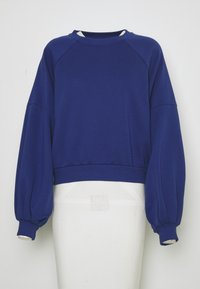 Modrá mikina s dlouhými rukávy, balónkovými rukávy a žebrovanými manžetami, vystavená na bílém torso manekýna na jednoduchém pozadí.