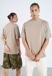 Könnyű, rövid ujjú póló, laza fazonnal. A modellen mintás zöld rövidnadrág van. Simább textúra, letisztult design, és nem látható logók.