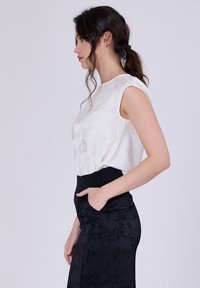 Blouse blanche sans manches avec un motif subtil, associée à une jupe noire ajustée avec des accents floraux texturés et des poches latérales.