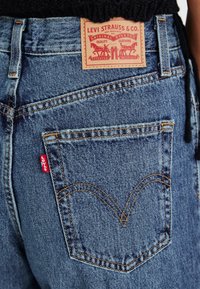 Blå denim jeans med en röd Levi's-tag, synlig sömnad och en bakficka med en böjd design. Läderlapp med varumärkeslogotyp ovanför.