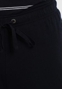 Pantalons de survêtement noirs avec un cordon de serrage, en coton doux, et une texture lisse sans motifs ni accents visibles.