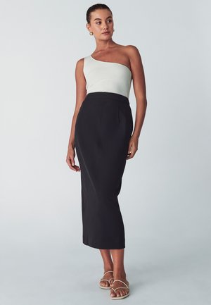 Groene geribbelde top met één schouder gecombineerd met een zwarte kokerrok. De rok heeft een getailleerde silhouette en verticale naden. Gecombineerd met lichte sandalen.