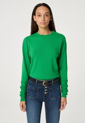 Groene lange mouwen top met een ronde hals, voorzien van subtiele schouderplooien en decoratieve knopen op de schouder, gecombineerd met high-waisted jeans.