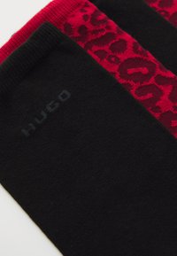 Närbild av svarta och röda strumpor med ett röd leopardmönster och en subtil "HUCO"-logotyp på det svarta tyget.