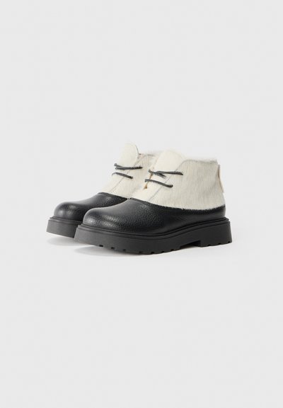 Svarta läderankelboots med en texturerad yta, vit pälsöverdela, svarta snören och en kraftig, räfflad gummisula.