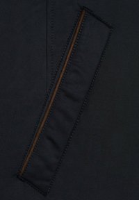 Czarna tkanina z ukośnym wzorem, z brązową kieszenią na zamek błyskawiczny zaakcentowaną kontrastowym przeszyciem i gładką teksturą.