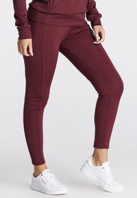 Bordeaux leggings i et strækbart stof med sidelommer, tætsiddende design og accentuerede sømme, parret med hvide sneakers.