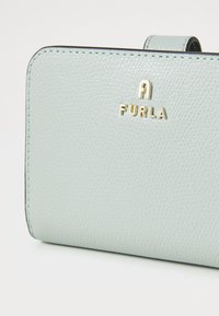 Lichtblauwe leren portemonnee met textuur en gouden hardware waarop de merknaam "Furla" staat, met een rechthoekige vorm en gladde randen.
