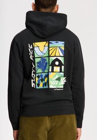 Felpa nera con cappuccio caratterizzata da un vivace design grafico sul retro, con quadrati che mostrano vari motivi e il testo "SLOW PACE" in bianco.