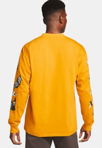 Cămașă galbenă cu mânecă lungă, confecționată din bumbac, cu imprimeuri de fluturi și insecte pe ambele mâneci. Textură netedă, guler rotund, croi lejer.