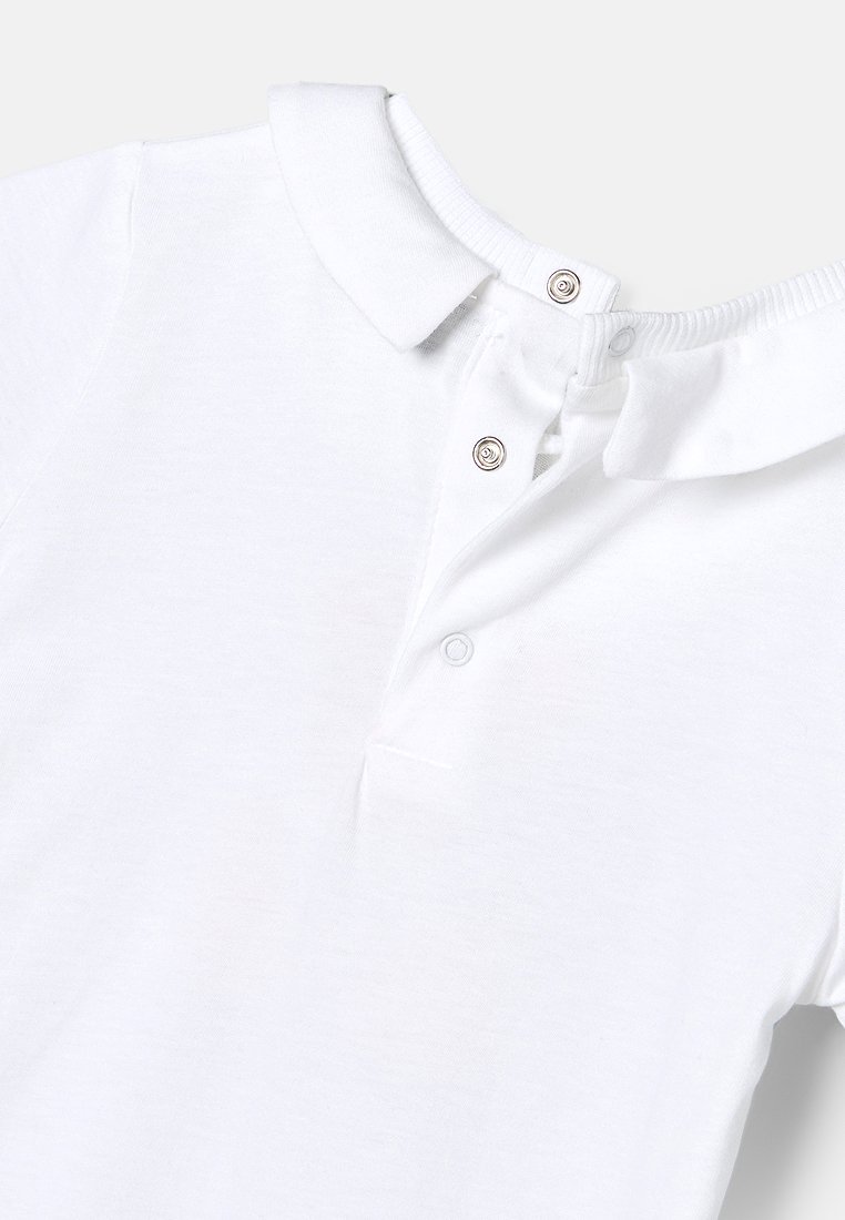 Polo shirt blanc en coton avec des manches courtes, un col, et trois boutons-pression sur la patte de boutonnage. Texture lisse.