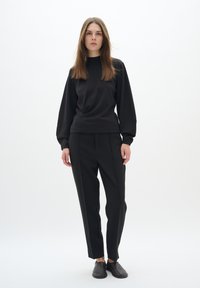 Black sweatshirt with long sleeves, paired with tailored black pants. Smooth fabric, minimalist design, and a modern silhouette.