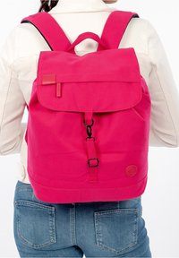 Růžový plátěný batoh s klopou, nastavitelnými popruhy a přední sponou. Obsahuje logo nášivku na spodní části a hladký povrch.