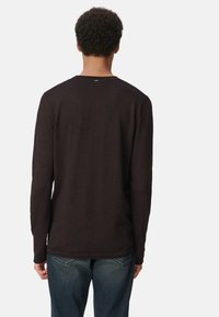 T-shirt à manches longues, marron foncé, avec une texture côtelée, un col rond et un ourlet plat, porté avec un jean bleu. La vue de dos ne montre aucun logo.
