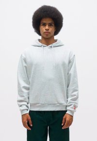 Felpa grigia in un mix di cotone, con cappuccio, coulisse e polsini a costine. Abbinata a pantaloni verde scuro, indossata da una persona.