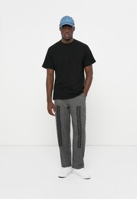 Black short-sleeve t-shirt, gray patterned trousers with black accents, white sneakers, and a light blue cap. Simple, modern design.