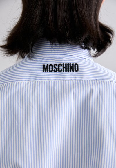 Gestreepte blauwe shirt met een kraag; voorzien van een zwarte geborduurde "MOSCHINO" op de rug. Gemaakt van een gladde stof met een lichte textuur.