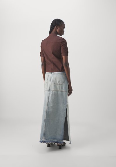 Bruine kortemedes shirt met hoge kraag, gecombineerd met een lange lichtblauwe denimrok met zijsplitten en zichtbare achterzakken.