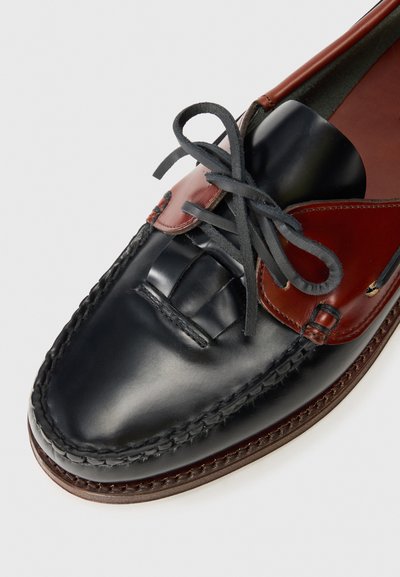 Zapato de vestir de cuero negro y marrón con cordones negros atados en un lazo y costuras detalladas a lo largo de los bordes.