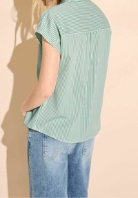 Chemise à manches courtes rayée verte et blanche avec un empiècement au dos, assortie à un jean large bleu clair, présentant une texture de tissu douce.