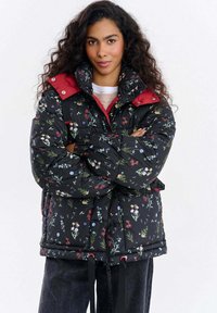 Pikowana kwiecista kurtka w kolorze czarnym z czerwonym kołnierzem, posiadająca sznurek ściągający u dołu, wielokolorowe wzory kwiatowe oraz zamek błyskawiczny.