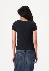 Tamsiai mėlyna trumpomis rankovėmis viršūnė su apvalia iškirpte, pasižyminti tekstūruota medžiaga ir neapdorotais kraštais, derinama su džinsine sijonu, turinčiu užpakalines kišenes.