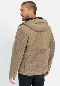 Brun fleecejakke med en quiltet beige front og hætte, der har struktureret stof, kontrastfarvede ærmer og et logo-patch på armen.