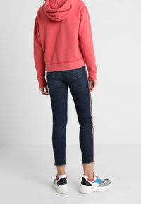Rode cropped hoodie met een trekkoord, gecombineerd met donkere skinny jeans met zijstrepen en rafelige zomen. Draagt het met multicolore sneakers.