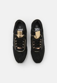 Chaussures de sport noires avec une tige texturée, des accents dorés et des lacets noirs. Dotées d'un col matelassé et d'une semelle blanche pour le confort.