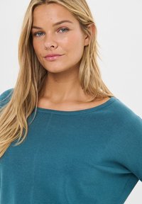 Maglione a maglia color teal con scollatura ampia e maniche lunghe, caratterizzato da una texture morbida e una vestibilità comoda.