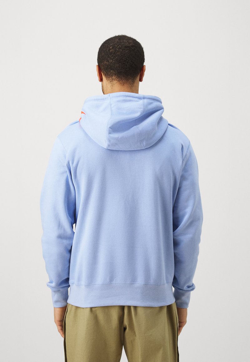 Sudadera azul claro con un acabado texturizado, capucha ajustable con cordones y puños acanalados. Presenta un acento contrastante cerca de la capucha.