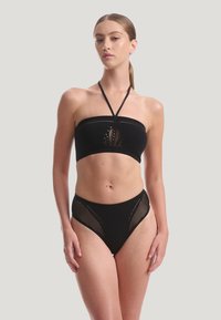 Svart bandeau-bikinitopp med perforerat mönster och halterneckband, kombinerad med svarta högmidjade bikiniunderdelar med meshdetaljer.
