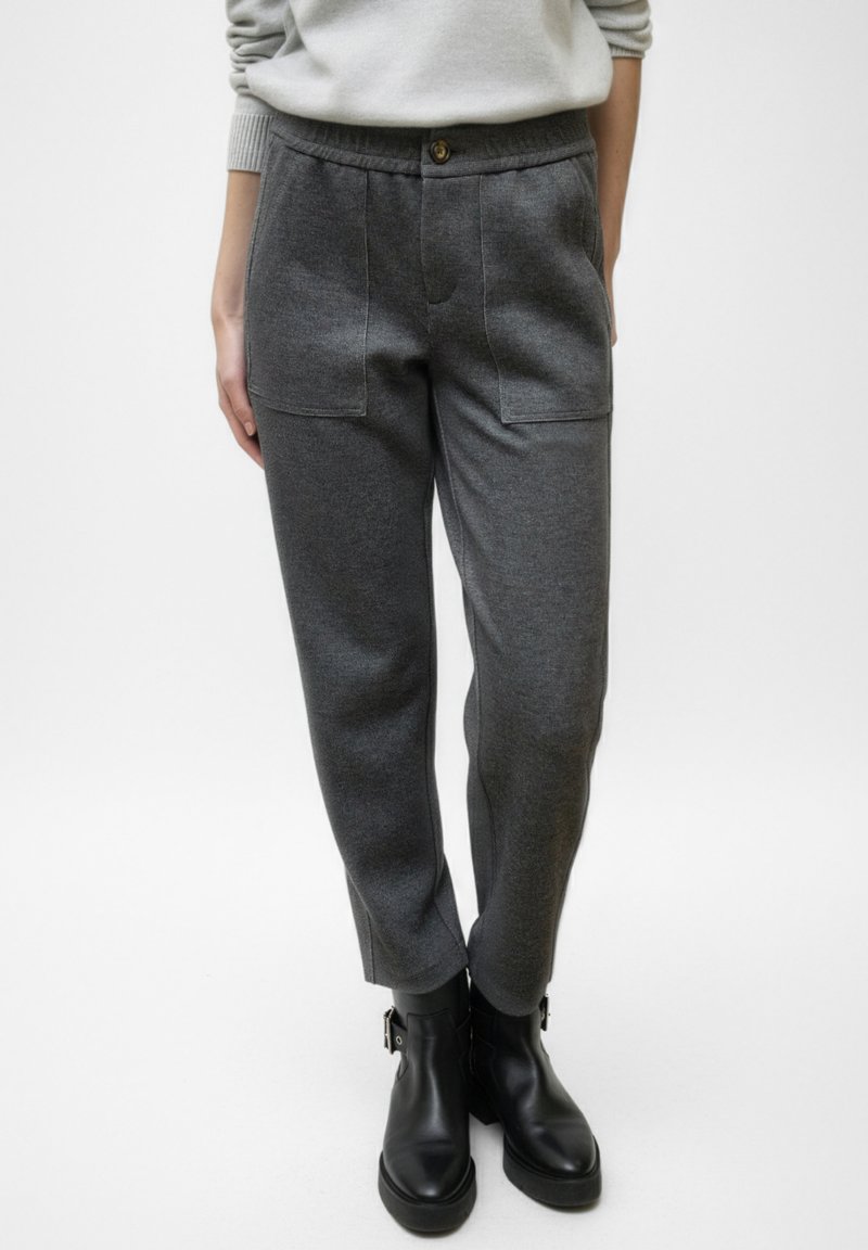 Pantalones grises de talle alto hechos de material suave, con dos bolsillos delanteros y cierre de botón. Combinados con botas negras hasta el tobillo.