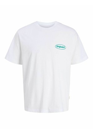 Adolescent garçon aux cheveux bouclés, debout en souriant, portant un t-shirt blanc avec un petit logo, un jean bleu foncé et des baskets noires avec des lacets blancs.