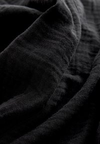 Tessuto nero, che mostra una texture morbida con leggere creste e pieghe. Il materiale appare leggero e si drappeggia con fluidità.