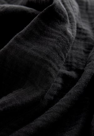 Czarna tkanina o miękkiej fakturze z subtelnymi prążkami i fałdami. Materiał wydaje się lekki i gładko się układa.