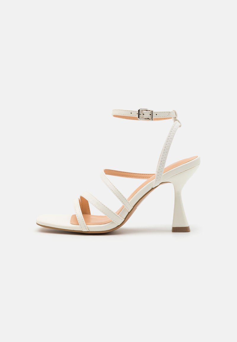 White strappy high-heeled sandal with an ankle buckle, smooth texture, square toe, and a sculpted heel. Light beige insole.
