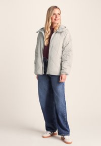 Light gray quilted jacket with a hood, zip front, and two side pockets, paired with blue wide-leg jeans and white sneakers.
