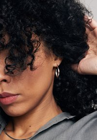 Srebrna kolczyk w kształcie kółka na zbliżeniu twarzy z ciemnymi kręconymi włosami. Skóra ma gładką teksturę, a usta w-neutralnym kolorze.