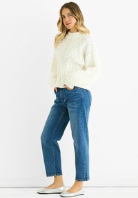 White cable-knit sweater with textured patterns, relaxed fit; paired with cropped blue jeans and silver ballet flats.