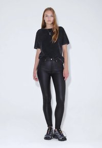 Černé tričko s krátkými rukávy, doplněné o černé legíny z umělé kůže s vysokým pasem. Obuv představují černé tenisky s barevnými doplňky.