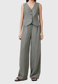 Šedý lněný vestový a široký kalhotový set. Vesta má výstřih do V, bez rukávů a pět předních knoflíků. Volný střih s měkkou strukturou.