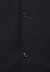 Due bottoni neri cuciti su un capo di tessuto nero con cuciture verticali lungo la linea dei bottoni.