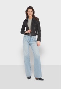 Giacca da moto in pelle nera con colletto, t-shirt grigia sotto e jeans a gamba larga blu chiaro. Gli stivaletti neri a punta completano il look.