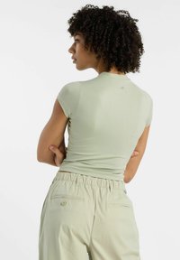 Lys grøn tætsiddende t-shirt med korte ærmer, glat tekstur og et lille logo på ryggen. Båret med matchende lyse bukser.